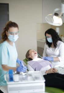 A dentist and dental hygienist work together to clean the teeth of a dental patient reclined in the dental chair.